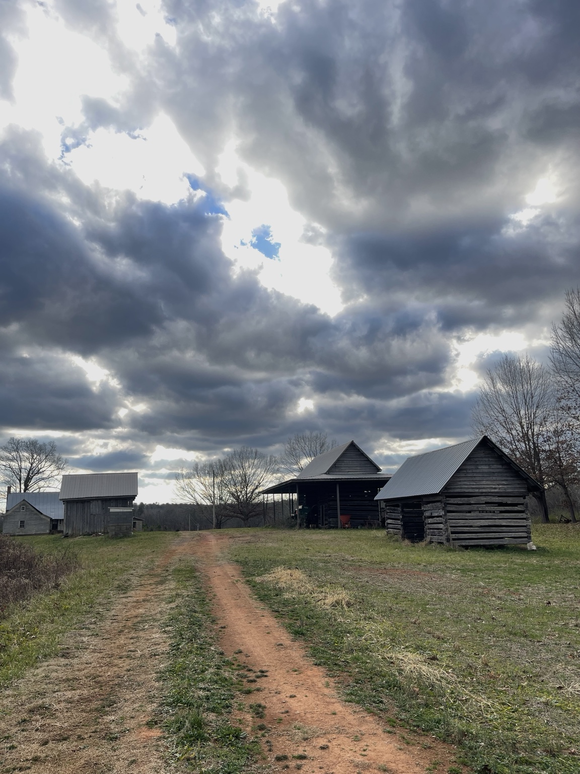 Historic outbuildings at Lilly beside a red-dirt lane beneath a dramatic cloudy sky