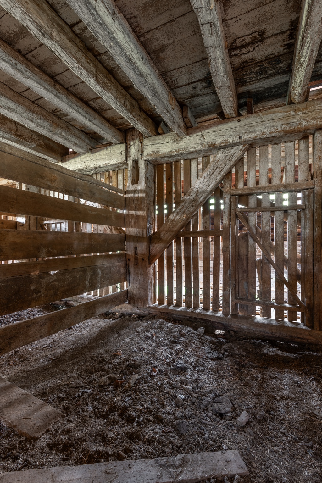 Interior of a historic timber structure with heavy ceiling beams, diagonal bracing, wooden stall partitions and a plank door