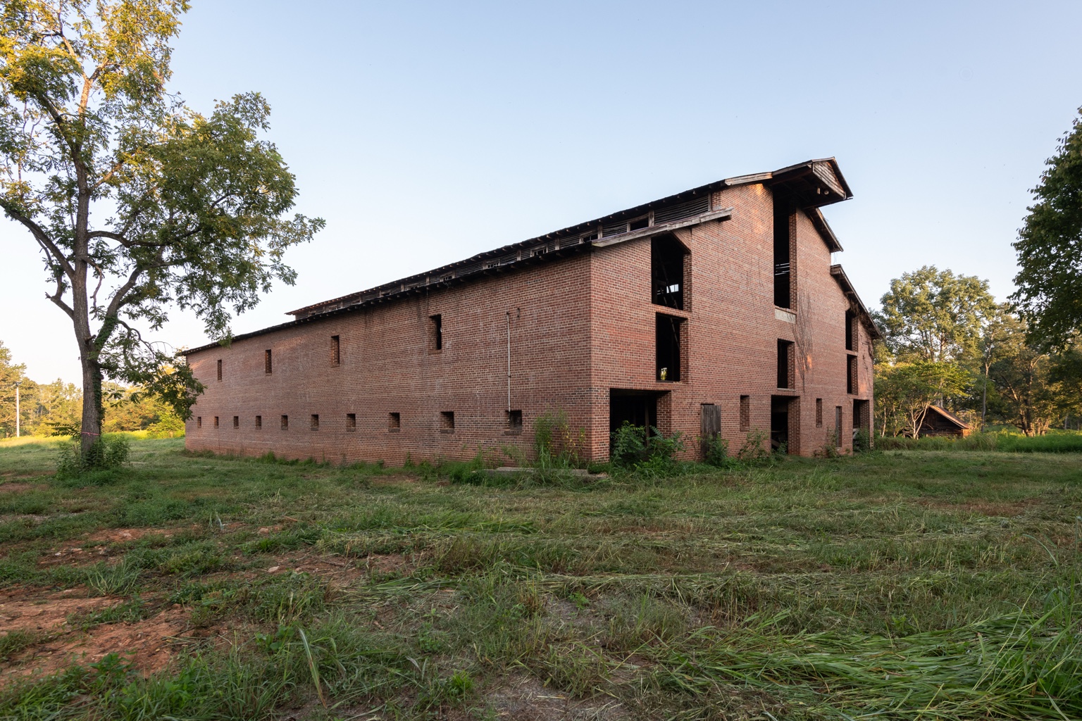 Exterior of the 1931 Mule Barn, showing its long red-brick walls and tall open bays among trees at Carpenter Preserve